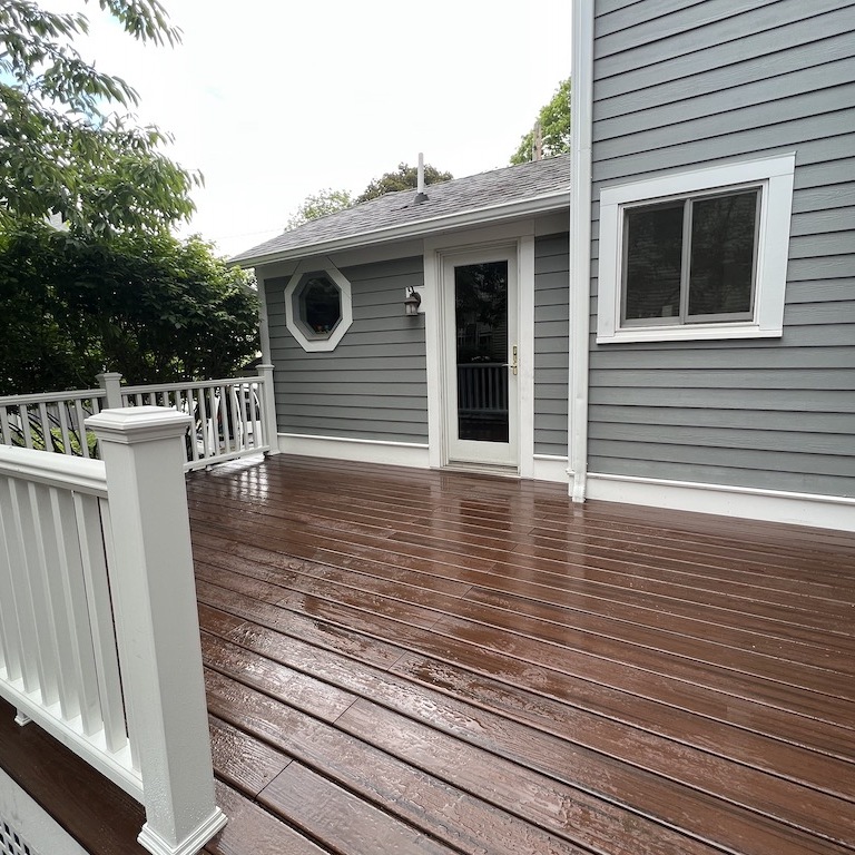 Another view of the same newly-built wooden patio, now focusing on the white rails framing the patio and another side door.